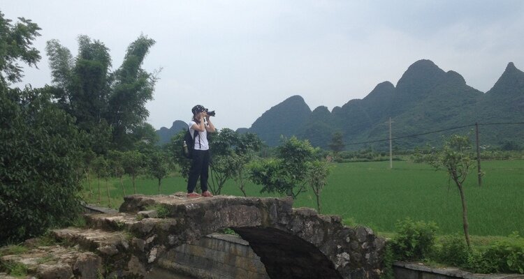 A tourist is taking photos on the ancient stone arch bridge in Yangshuo.