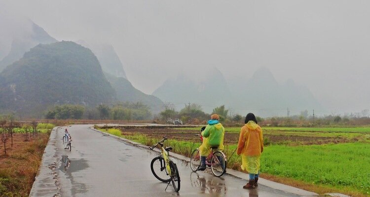 On a rainy spring day, two guests wearing colorful plastic raincoats were riding bicycles in the countryside of Yangshuo.
