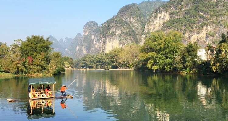 A boatman poles a bamboo raft, taking a boatload of passengers on a cruise on the Yulong River in Yangshuo