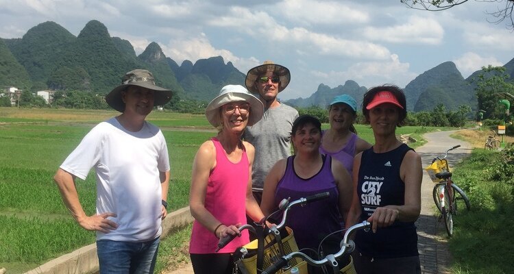 Six tourists dressed in light summer clothes pose for a group photo while cycling through the countryside of Yangshuo in the summer.