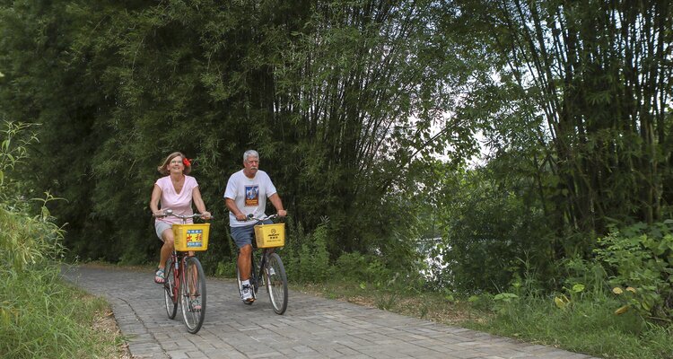 A couple of cycling enthusiasts, dressed in short sleeves and shorts, are riding their bicycles along the scenic banks of the Yulong River.
