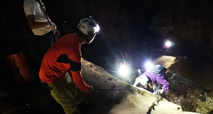 A couple of persons are caving in a dark and pristine cave only with headlights and a professional guide in Guilin