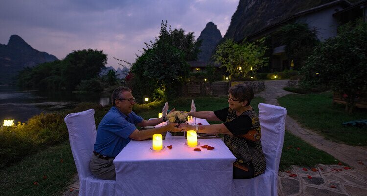 A Senior Couple are having a riverside dinner by the Yulong River in Yangshuo Mountain Retreat hotel