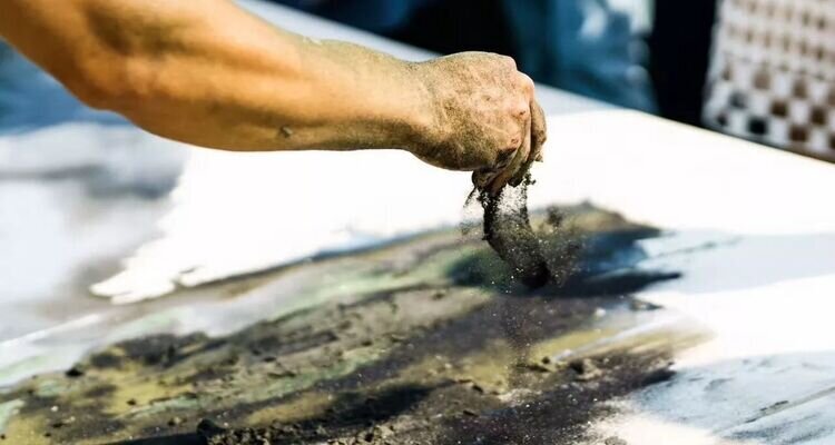 A man's hand is scattering sand to create a painting; Zhangjiajie Junsheng Sand Painting.