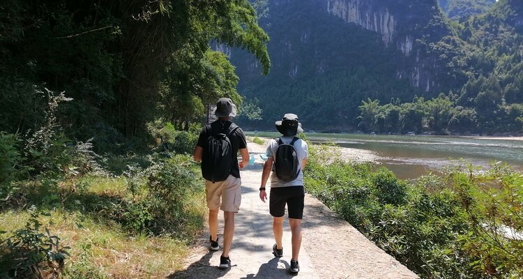 A couple of hiking enthusiasts, dressed in short sleeves and shorts, are hiking along the scenic banks of the Li River.
