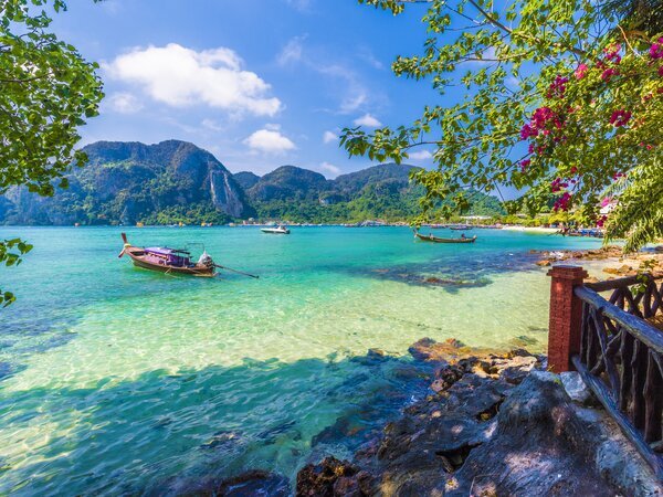 Spiaggia tropicale di Phuket con mare turchese e barche tradizionali thailandesi